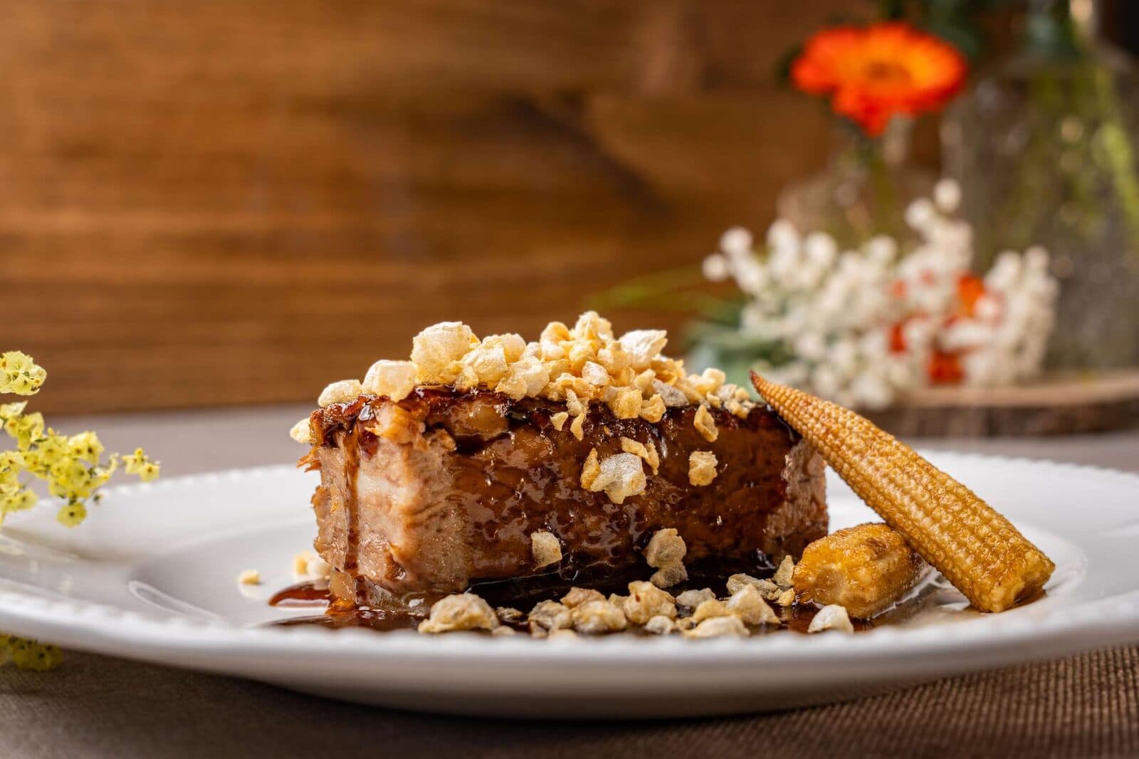 Plato de autor del catering de El Cachirulo: carne glaseada con crujiente y mazorca, sobre plato blanco