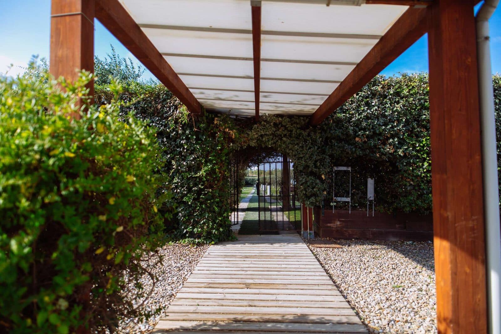 Pérgola de madera y pasarela de acceso al Pabellón de Ceremonias, entre hiedra y jardines