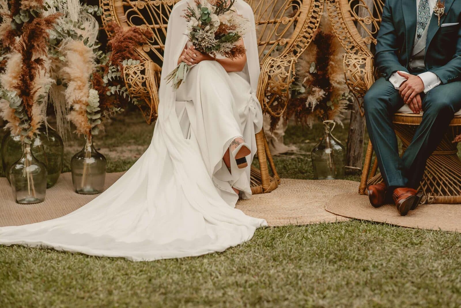 Una pareja de novios sentada en sillones de mimbre durante su ceremonia en el jardín